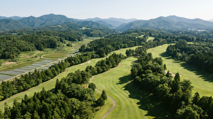 森と田畑に囲まれた日本の丘陵ゴルフ場の空撮風景（AI生成イメージ）